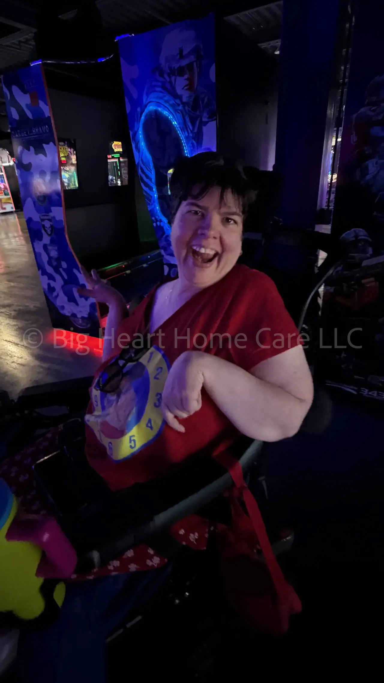 Big Heart Group Home resident smiling brightly while enjoying an arcade outing at ELEV8 Fun Tampa surrounded by colorful neon lights.