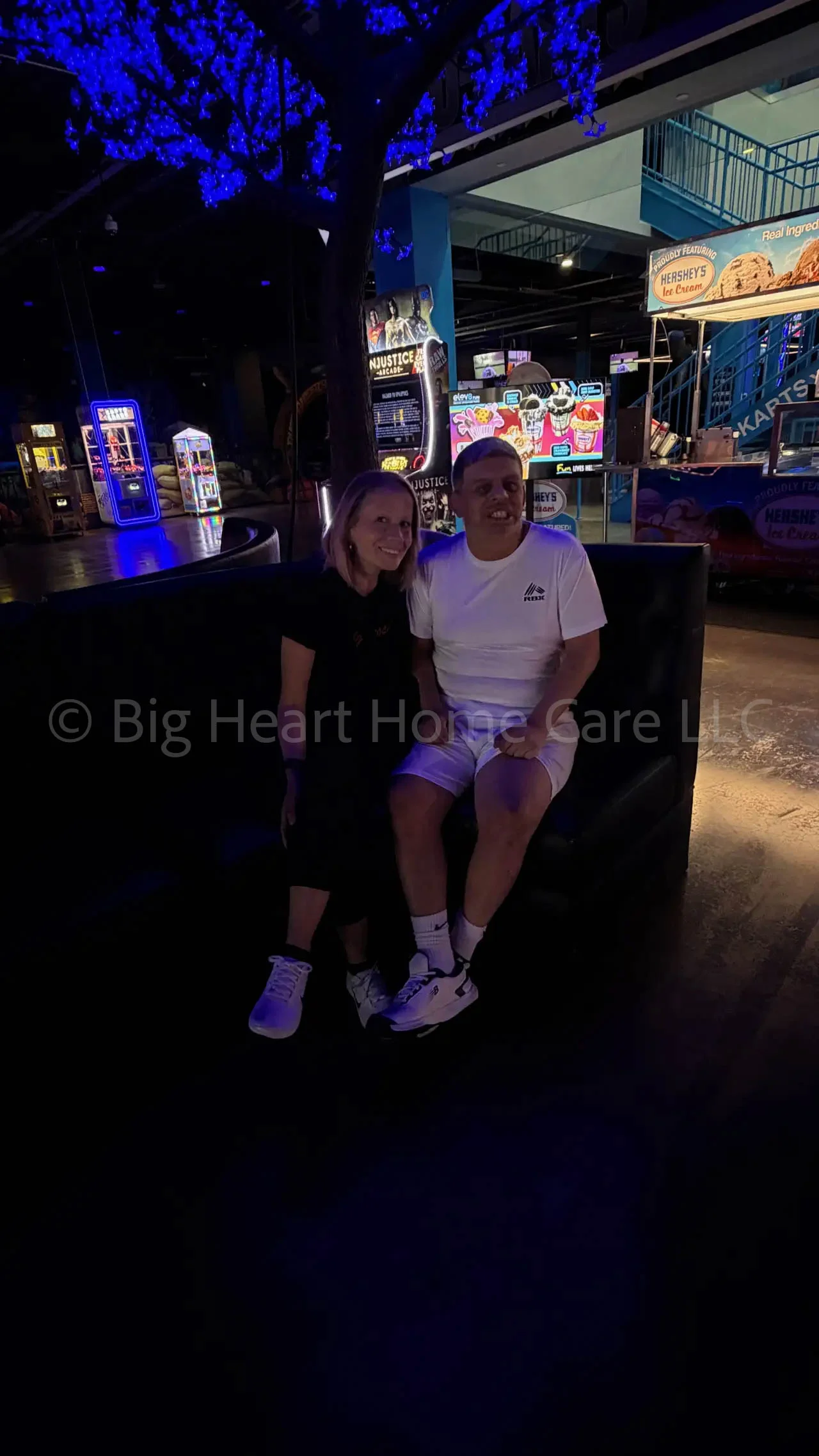 Big Heart Group Home resident and staff member sitting together on a couch at ELEV8 Fun Tampa surrounded by arcade lights in Tampa, Florida.
